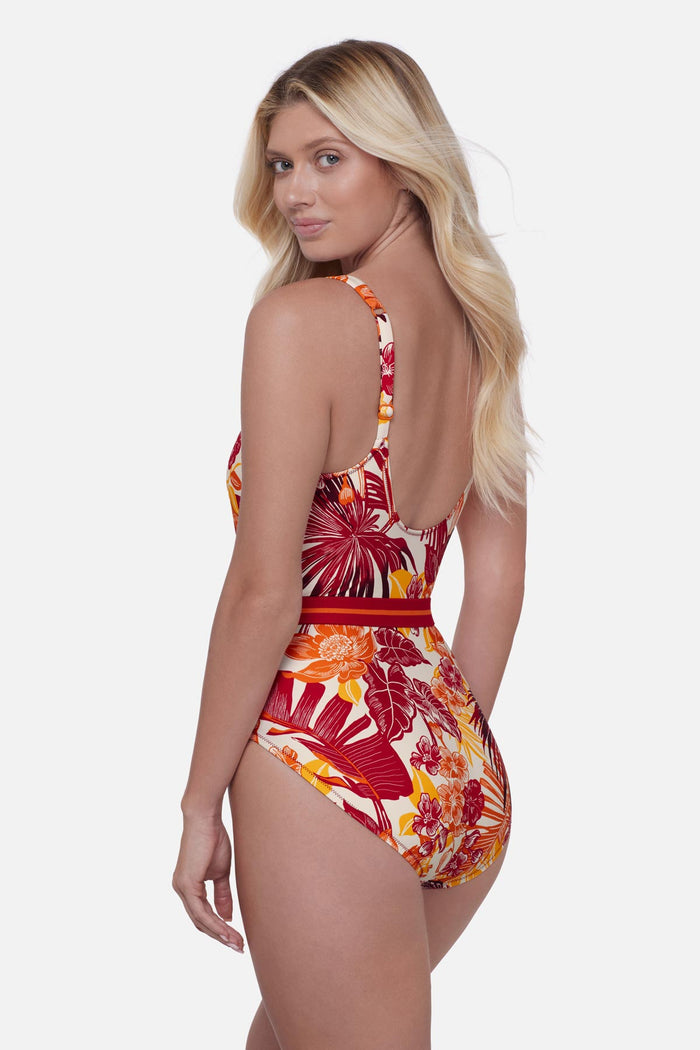 Woman turned left wearing a multicolored palm leaf printed one-piece swimsuit with a belt